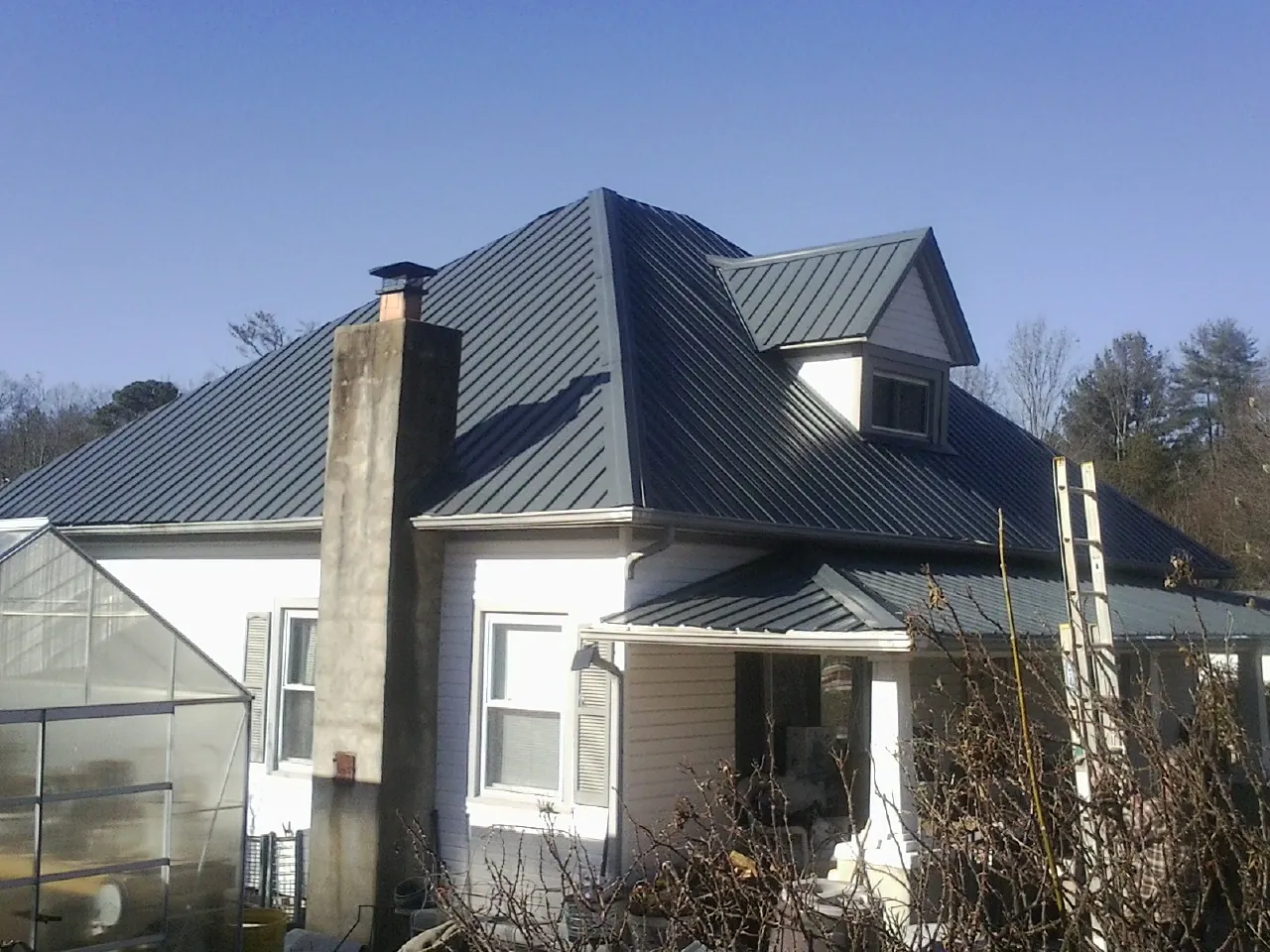 Dark blue standing seam metal roof on a white farmhouse with dormer — Slate & Tile Roof Repair by Roofing Brothers in Six Mile