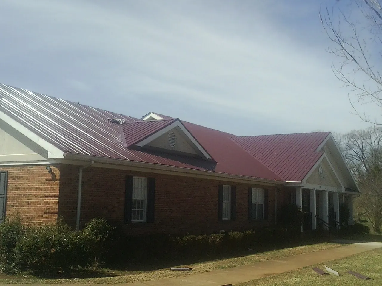 Red metal roof with gabled entries on a long brick building, from a Hail Damage Roof Repair job in Six Mile