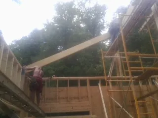 Carpenter raising a rafter beam on a new second story frame in Six Mile