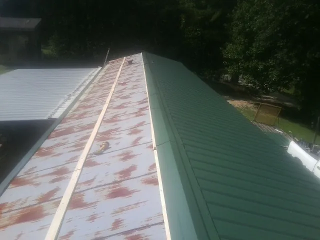 Old rusted panels beside newly installed green metal roofing — Wind Damage Roof Repair by Roofing Brothers in Six Mile