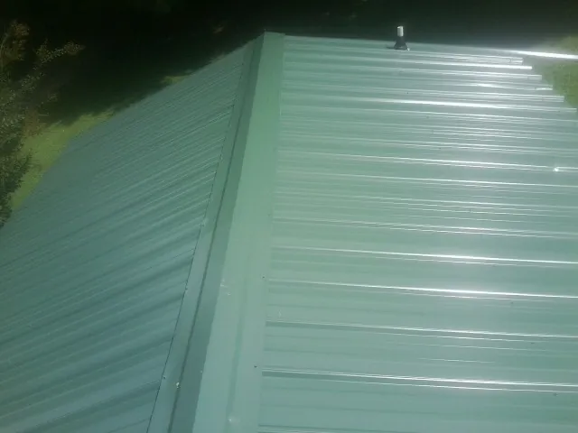 New green metal panels meeting at the ridge of a roof — Flat Roof Repair work by our crew in Six Mile
