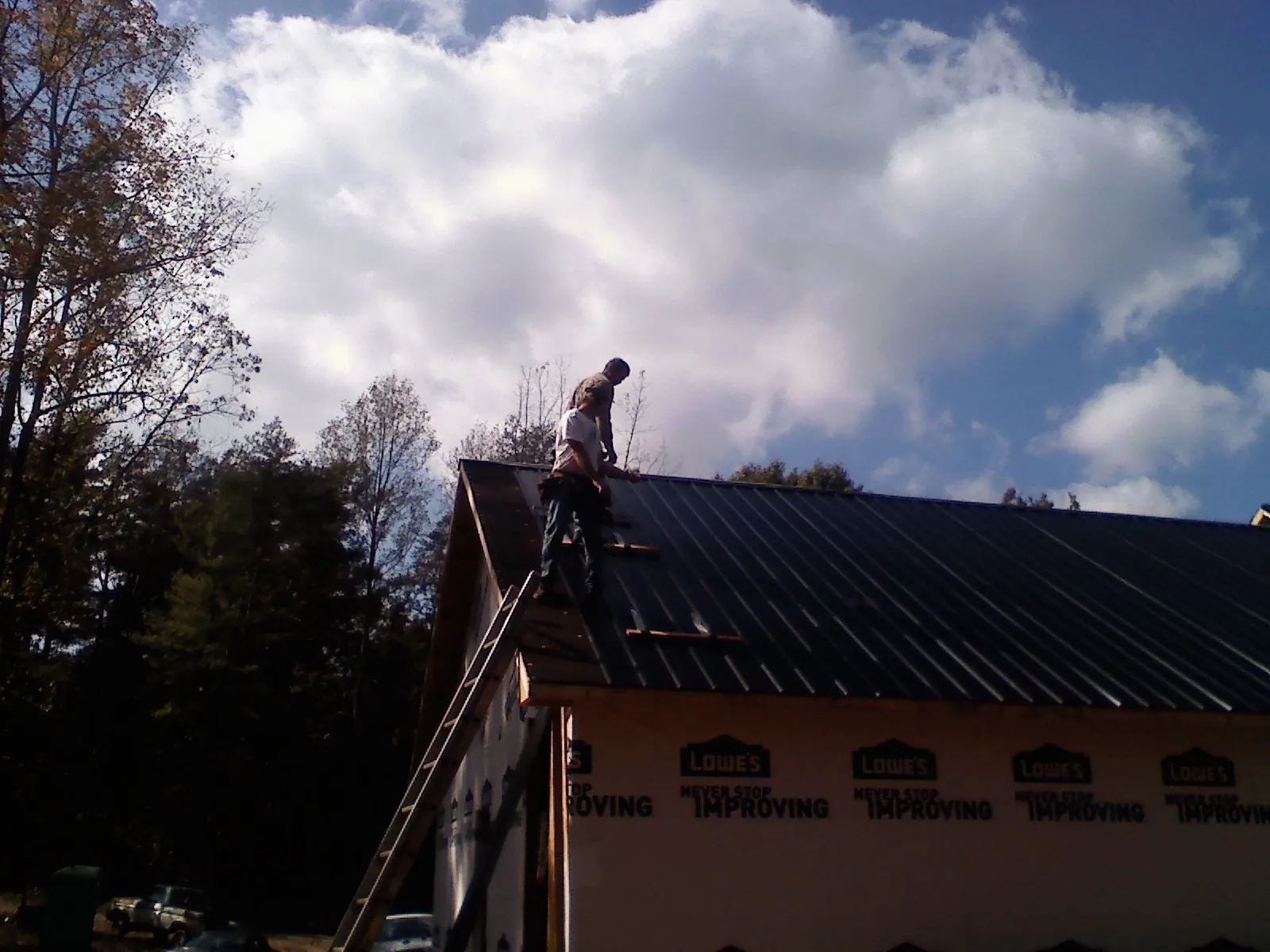 Roofer fastening dark metal panels high against a cloudy sky, from a Roof Inspection job in Six Mile