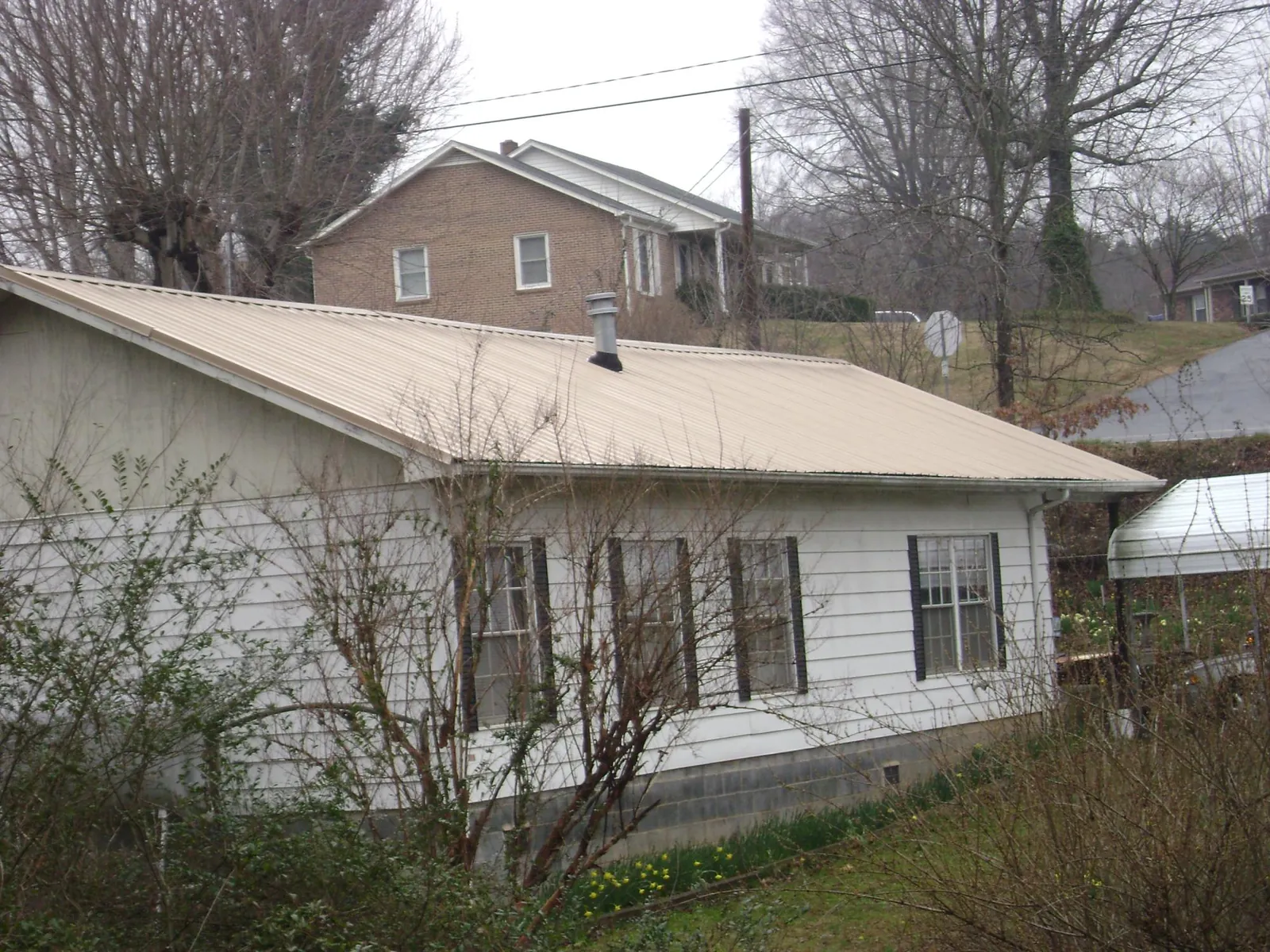 Tan metal roof on a white sided house set into a hillside — Commercial Roofing by Roofing Brothers in Six Mile