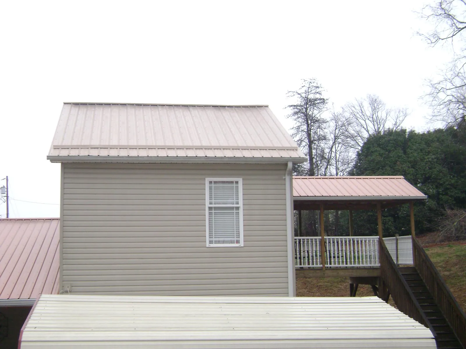 Tan metal roofs on a two story addition and attached porch, from a Roof Replacement job in Six Mile